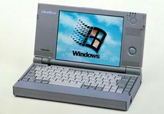 an old laptop computer sitting on top of a white surface with windows logo on the screen