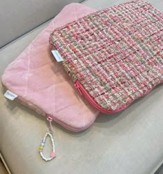 a pink purse sitting on top of a couch next to a white pillow and beaded bracelet