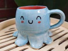 a blue ceramic cup with an octopus face on it's side sitting on a bamboo tray