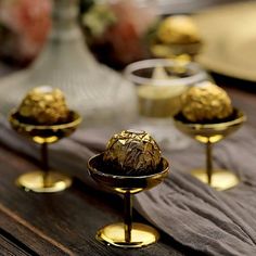 four gold candles sitting on top of a wooden table next to some vases with flowers in them