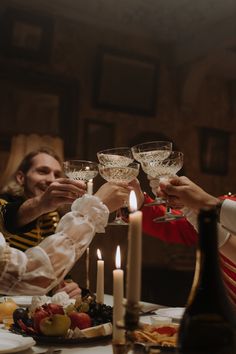 three people toasting with wine glasses in front of candles and fruit on the table