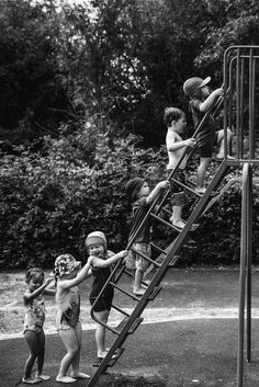 black and white photograph of children playing on a playground slide with trees in the background