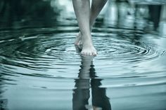 a person's feet in the water with their reflection on the wet surface,