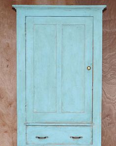 an old blue cabinet with two doors on the front and one door open, against a wooden wall