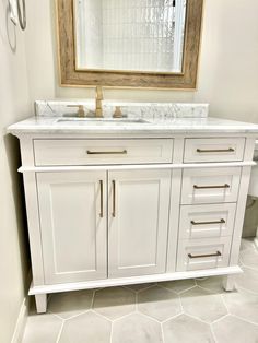 a white bathroom vanity with marble top and gold hardware on the handles, under a large mirror