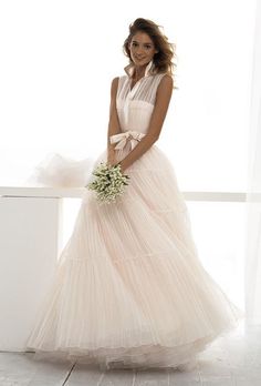 a woman in a wedding dress standing next to a window with her hands on her hips