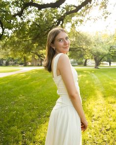 a woman in a white dress is standing on the grass and looking off into the distance