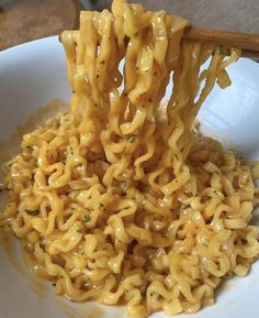 the noodles are being held up by chopsticks in a white bowl with yellow sauce