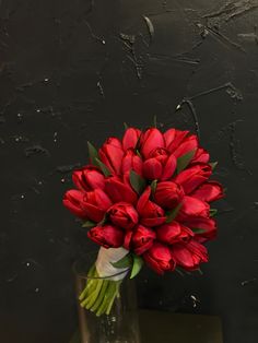 a bouquet of red tulips in a clear vase on a black table top