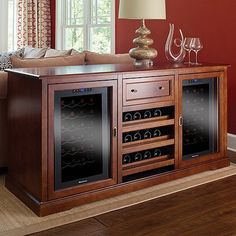 a wooden cabinet with wine bottles and glasses on it in front of a red wall