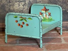 a small blue bed with mushrooms painted on the top and bottom side, sitting on a brick floor in front of a stone wall