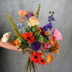 a person holding a bouquet of flowers in their hand on a gray wall behind them