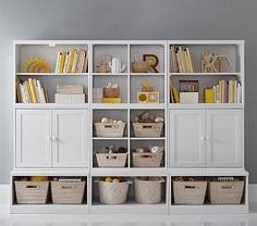 a white bookcase filled with lots of books and baskets next to a wall mounted clock