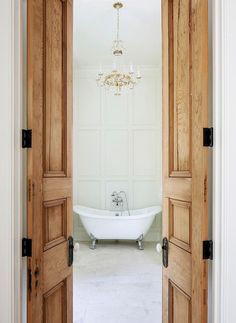 an open door leading to a bathroom with a tub and chandelier