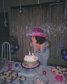 a woman wearing a pink hat blowing out the candles on her birthday cake at a party