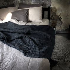 an unmade bed with blankets and pillows on it in a room that has stone walls