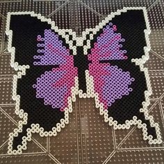 a butterfly made out of perler beads sitting on top of a metal tablecloth