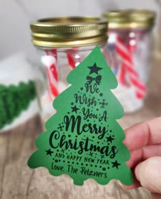 a hand holding a green christmas tree shaped gift tag in front of some candy canes