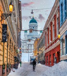 a person riding a bike down a snow covered street in front of buildings and a domed building