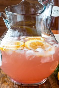 a pitcher filled with pink liquid and lemons on top of a wooden table next to bottles