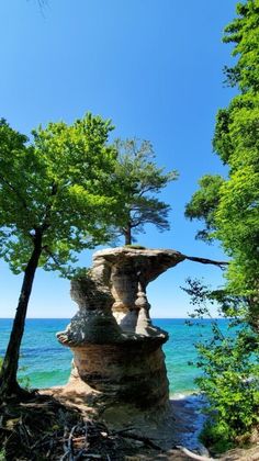 a rock formation in the middle of some trees by the water with blue sky and clouds