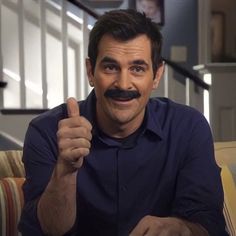 a man with a moustache giving the thumbs up