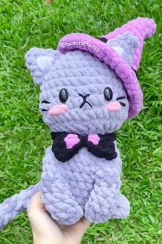 a person holding up a small crocheted cat in the grass with a hat on