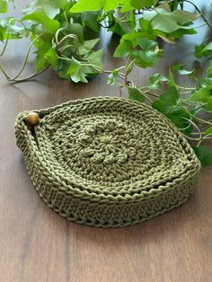 a green crocheted basket sitting on top of a wooden table next to plants