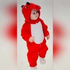 a baby dressed in a red and white animal costume is standing on one leg with his foot up to the ground