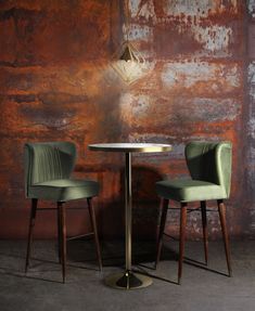 two green chairs sitting at a round table in front of a rusted brick wall