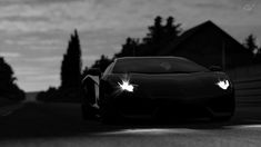 a black and white photo of a car driving down the road at night with headlights on