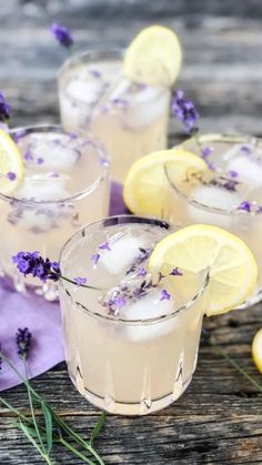 three glasses filled with lavender lemonade on top of a wooden table next to sliced lemons