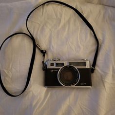 an old fashioned camera is laying on a white sheet with a black strap around it's neck