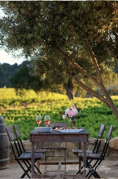 two wine glasses sitting on top of a wooden table next to a vase with flowers