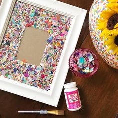 a white frame sitting on top of a wooden table next to a vase with sunflowers