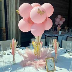 a table topped with lots of balloons and pink feathers on top of white clothed tables