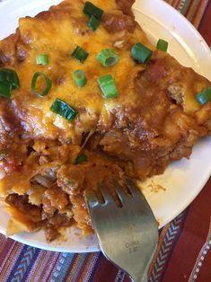 a white plate topped with lasagna covered in cheese and green onions next to a fork