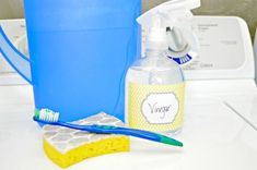 a blue bucket with a toothbrush next to a yellow sponge and a bottle of vinegar