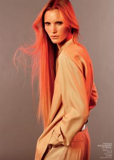 a woman with long red hair standing in front of a gray background