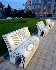 two white benches sitting next to each other on top of a cement slab in front of a building