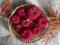 crocheted apples in a wicker basket on a wooden table next to dried flowers