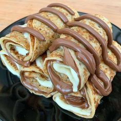 chocolate covered crepes on a black plate with white icing and drizzled