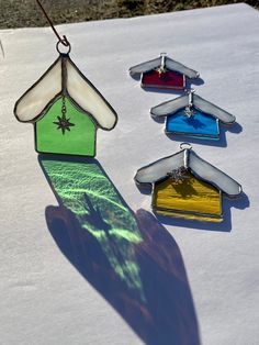 three stained glass birdhouses hanging from a string on a white table with snow and grass in the background