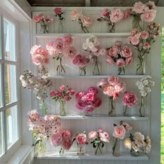 pink flowers are arranged on shelves in the window sill next to an open window