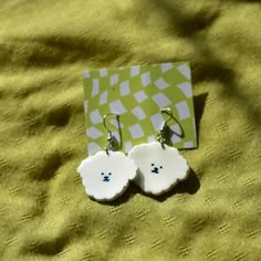 a pair of white earrings sitting on top of a green cloth covered table next to a card