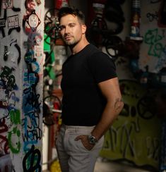 a man standing in front of a wall covered with graffitti and other graffiti