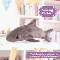 a stuffed shark laying on top of a table in front of a book shelf filled with books