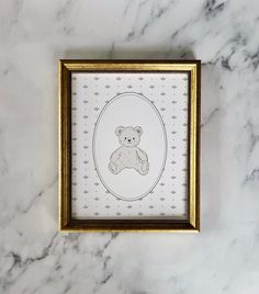 a framed drawing of a teddy bear on a marble surface