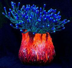 a colorful vase filled with lots of blue and orange flowers on top of a black background