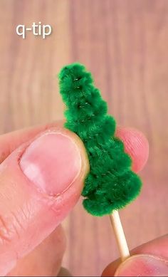 a tiny green christmas tree on a toothpick in someone's hand that is holding it